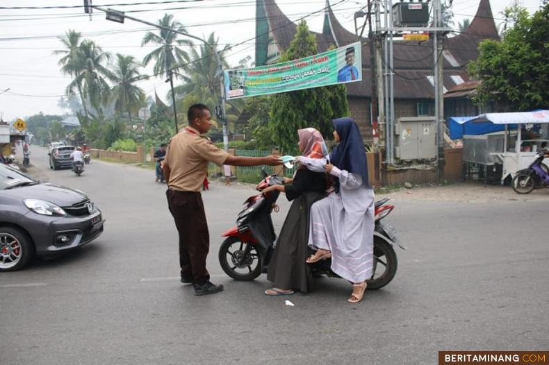 Seorang anggota Pramuka MAN 1 Solok sedang bagikan masker pada pengendara. Foto: fen
